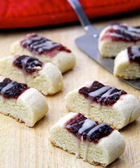 Five bar-shaped raspberry ribbon cookies sit on a table topped with raspberry jam