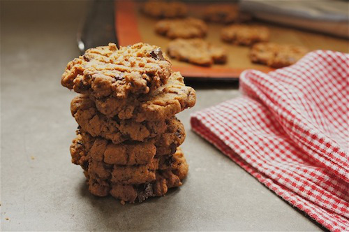 A stack of peanut butter chocolate chip cookies are on a table next to a checkered napkin