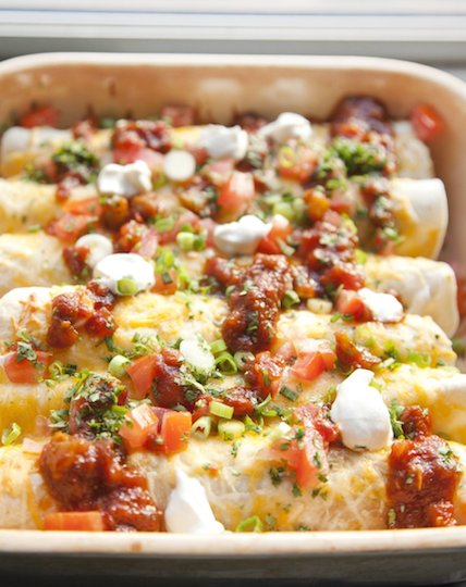 A platter of chicken enchiladas made from a crock pot are topped with sour cream