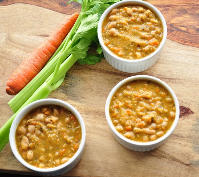 three bowls of white bean soup, cooked in a crock pot, sit beside a carrot and celery