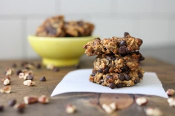 A stack of chunky, sugar free cookies sit on a napkin in front of a yellow bowl filled with more cookies