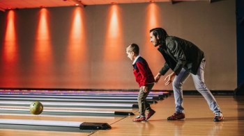 A young boy stands at the end of the lane, with his dad behind him at an Atlanta bowling alley