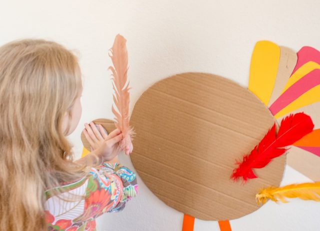 A girl holds a feather as she plays the Thanksgiving activity Pin the Feather on the Turkey