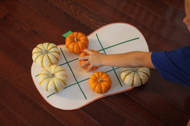 Mini pumpkins are set up on a tic tac toe board to provide a Thanksgiving activity