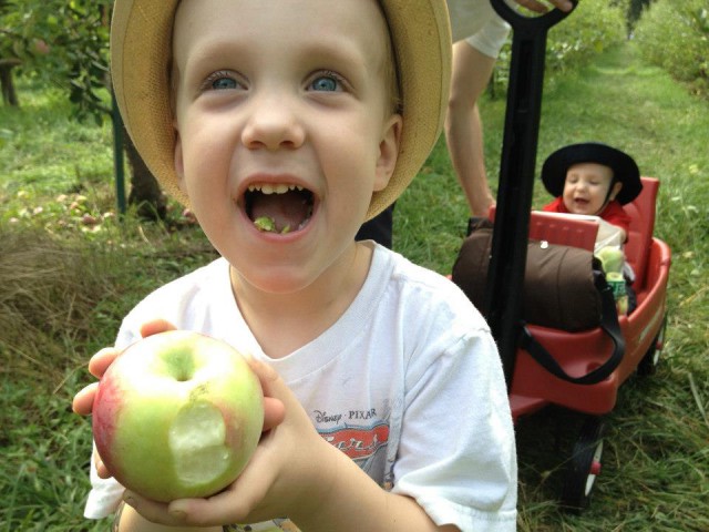 A little boy in a hat takes a bite out of an apple