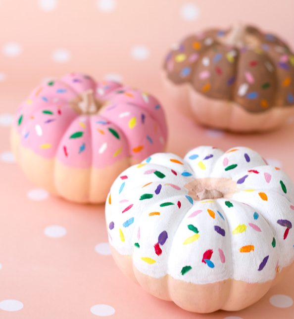 Three pumpkins are decorated like donuts