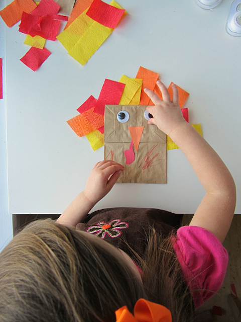 A girl completes a Thanksgiving crafting activity by making a brown paper bag into a turkey