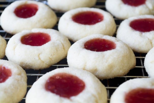 About a half dozen round white cookies each with a jam thumbprint in the middle