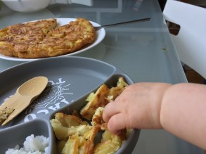 a baby's hand doing baby-led weaning by grabbing from a plate full of food