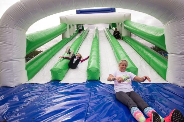 Two kids slide down an inflatable slide in an indoor playspace