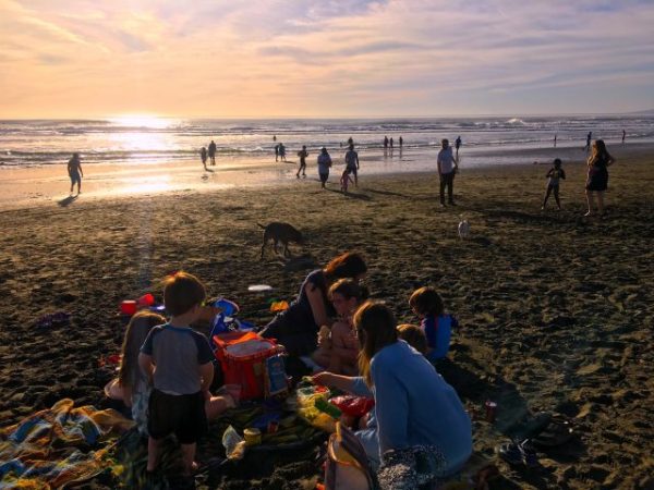 A group of people enjoy a beach picnic at sunset on Ocean Beach