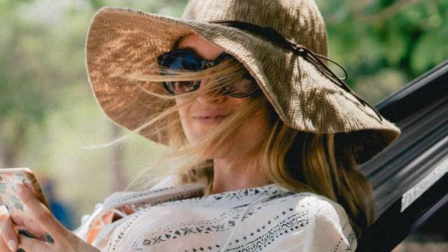 woman in hammock smiling and checking phone wearing sunhat and sunglasses - pregnant in summer