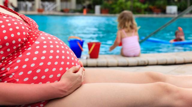 pregnant woman by a pool with kids playing in the pool-pregnant in summer