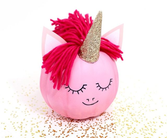 A pink pumpkin is decorated like a unicorn