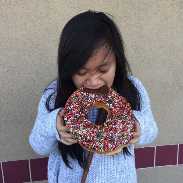A girl bites into a giant chocolate sprinkle donut