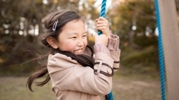 a girl swing from a tree swing during fall with leaves falling around