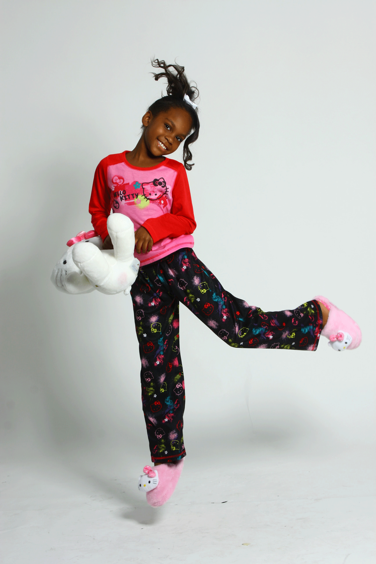 A little girl dressed in pink pajamas does a happy dance with her stuffed animal during a sleepover