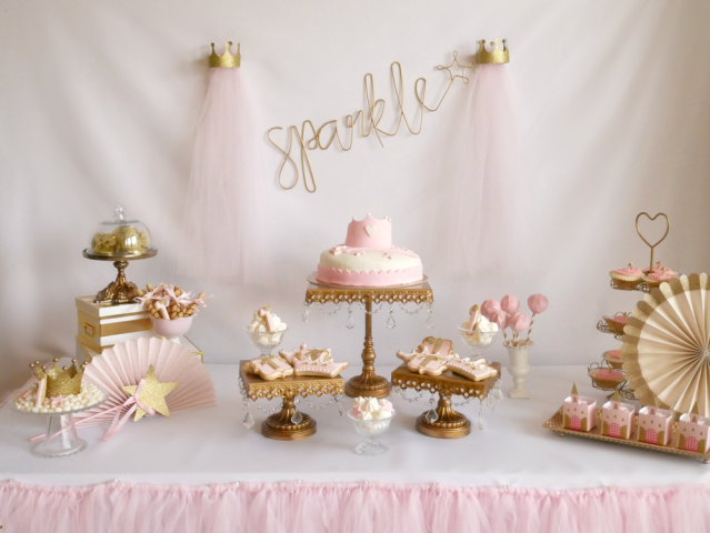 Pink cakes and tulle and other princess party decorations sit on a table waiting for the royal birthday party guests to arrive.