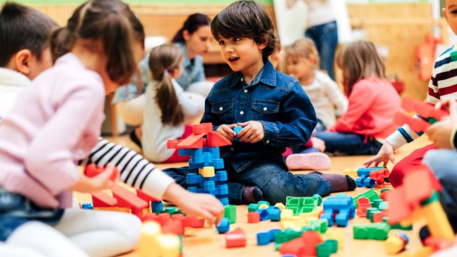 a kindergarten age boy plays with friends building with colorful blocks