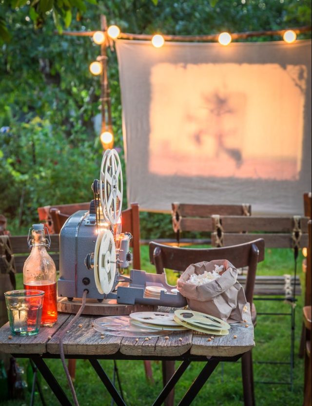 An outdoor movie screen and decorations are set up as part of an outdoor movie theme birthday party idea for kids