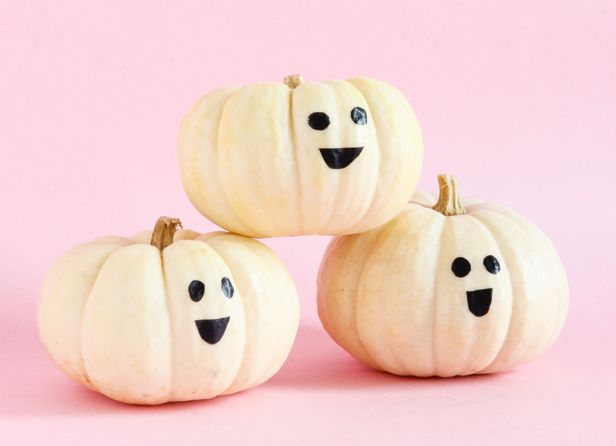Three white pumpkins are dresses as little ghosts for a happy ghost no-carve pumpkin decorating idea