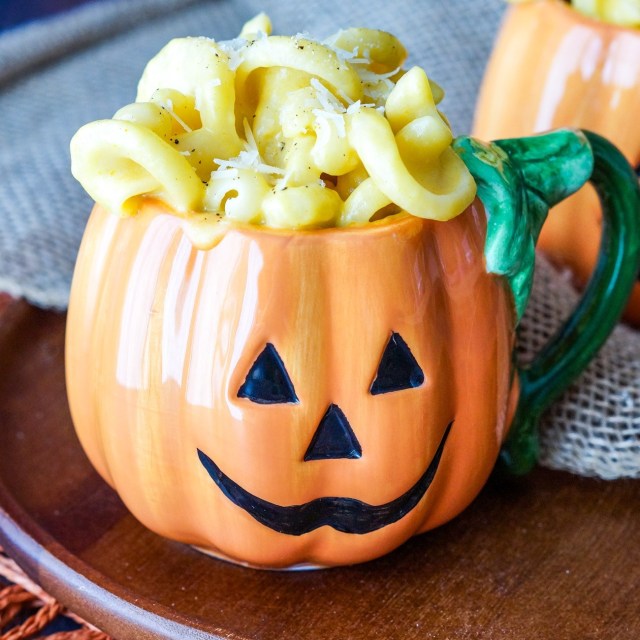 A jack-o-lantern cup is filled with pumpkin macaroni and cheese