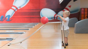 a young kid rolls a bowling ball down a ramp