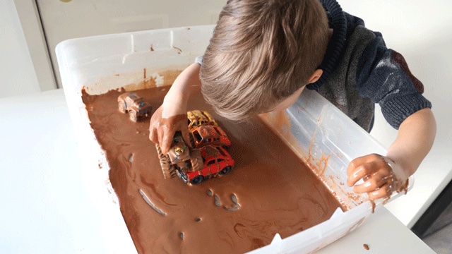 a boy plays with a truck in a sensory play box that's spring themed