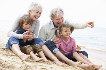 Grandparents sit on the beach with their two grandchildren
