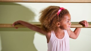 a young girl with pink ribbon rests again a ballet bar at a dance class for kids near portland, OR