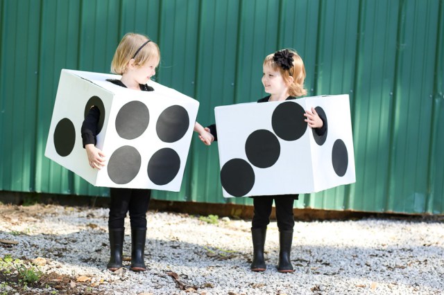 Two girls are dressed in matching Halloween costumes made of cardboard that make them look like a pair of die
