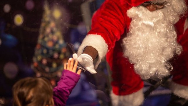 A child and Santa touch hands at Black Santa PDX when they take pictures with Santa in portland