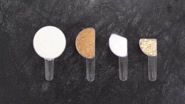 Measuring spoons with baking ingredients are lined up on a table