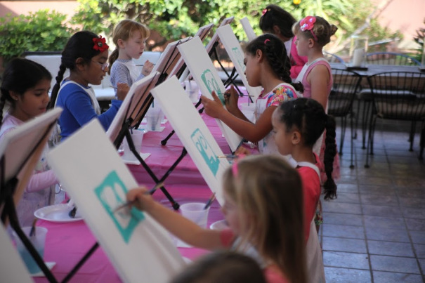 Two rows of children stand painting at easels during a mobile art birthday party