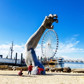 three children playing in front of hand sculpture with ferris wheel in the background