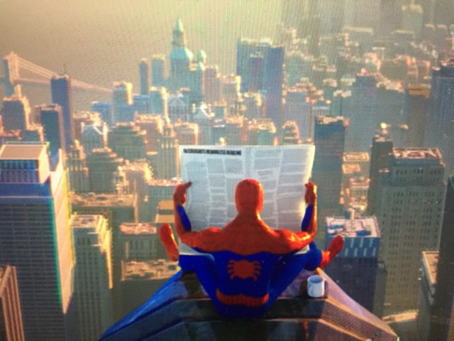 a mini Spider-Man figurine reading a newspaper on a balcony with the city skyline in front of him