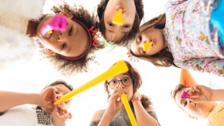 kids at a birthday party with party hats and whistles lean over the camera