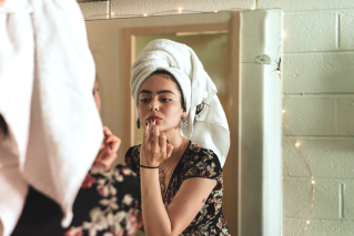 woman looking in mirror applying lip product