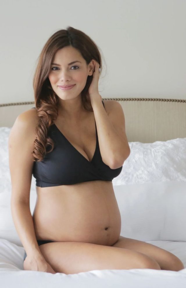 pregnant woman in black bra kneeling on bed