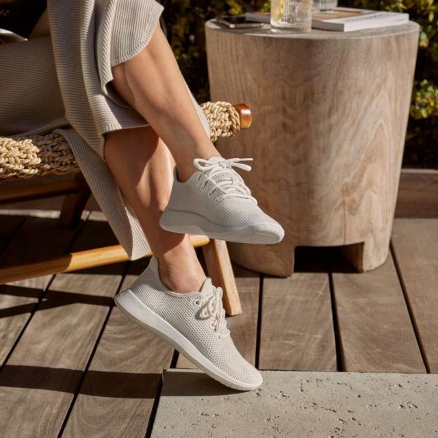 bottom half of a woman sitting on a patio deck wearing a pair of white allbirds tree runner sneakers