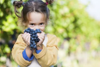 girl with pigtails holding grapes and smiling