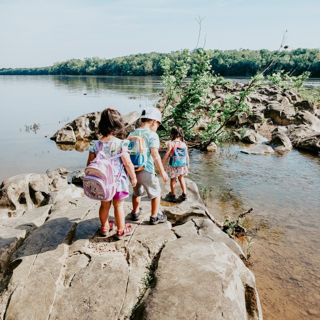 three children climbing on rocks near river in Virginia