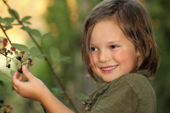 A girl smiles as she picks blackberries