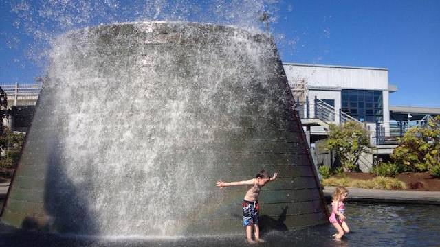 two kids splash in a fountain outside activities that looks like a submarine