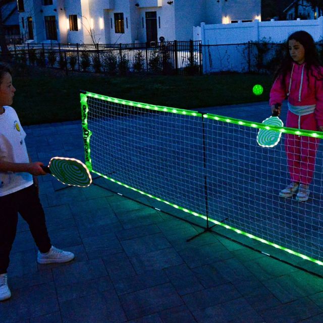 two kids playing with a glow-in-the-dark pickleball set