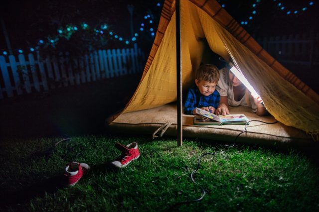 kid reading in a tent outside