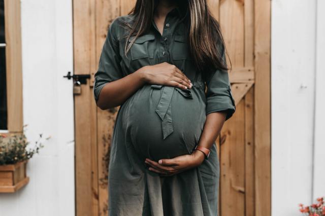 A mom to be in a green dress embraces her pregnant belly as she wonders how to tell the gender of her baby