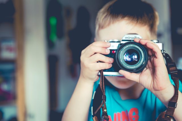 Young boy holding a camera and using his hand to focus