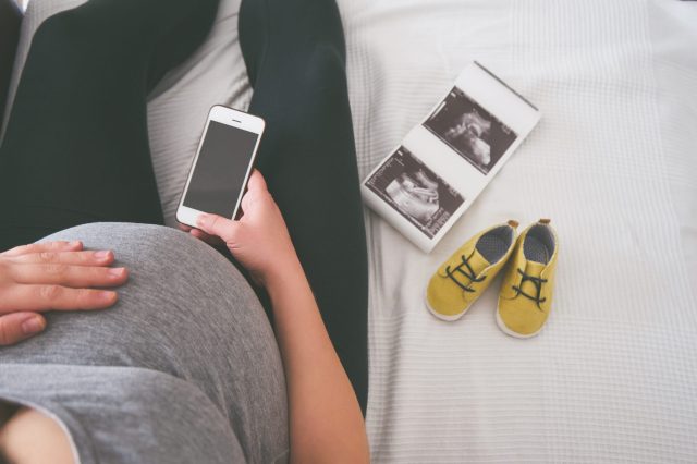Young pregnant woman relaxing on sofa with smart phone baby name inspiration
