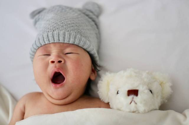 Asian baby yawning in bed next to stuffed animal - baby sleep guide